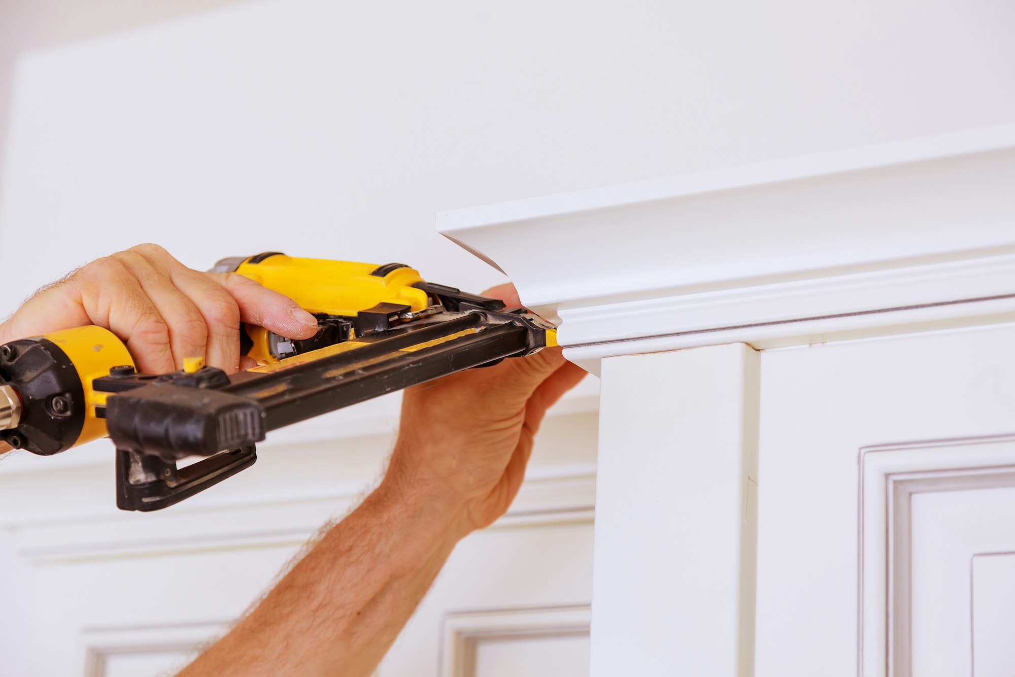 Carpenter brad using nail gun to Crown Moulding on kitchen cabinets framing trim